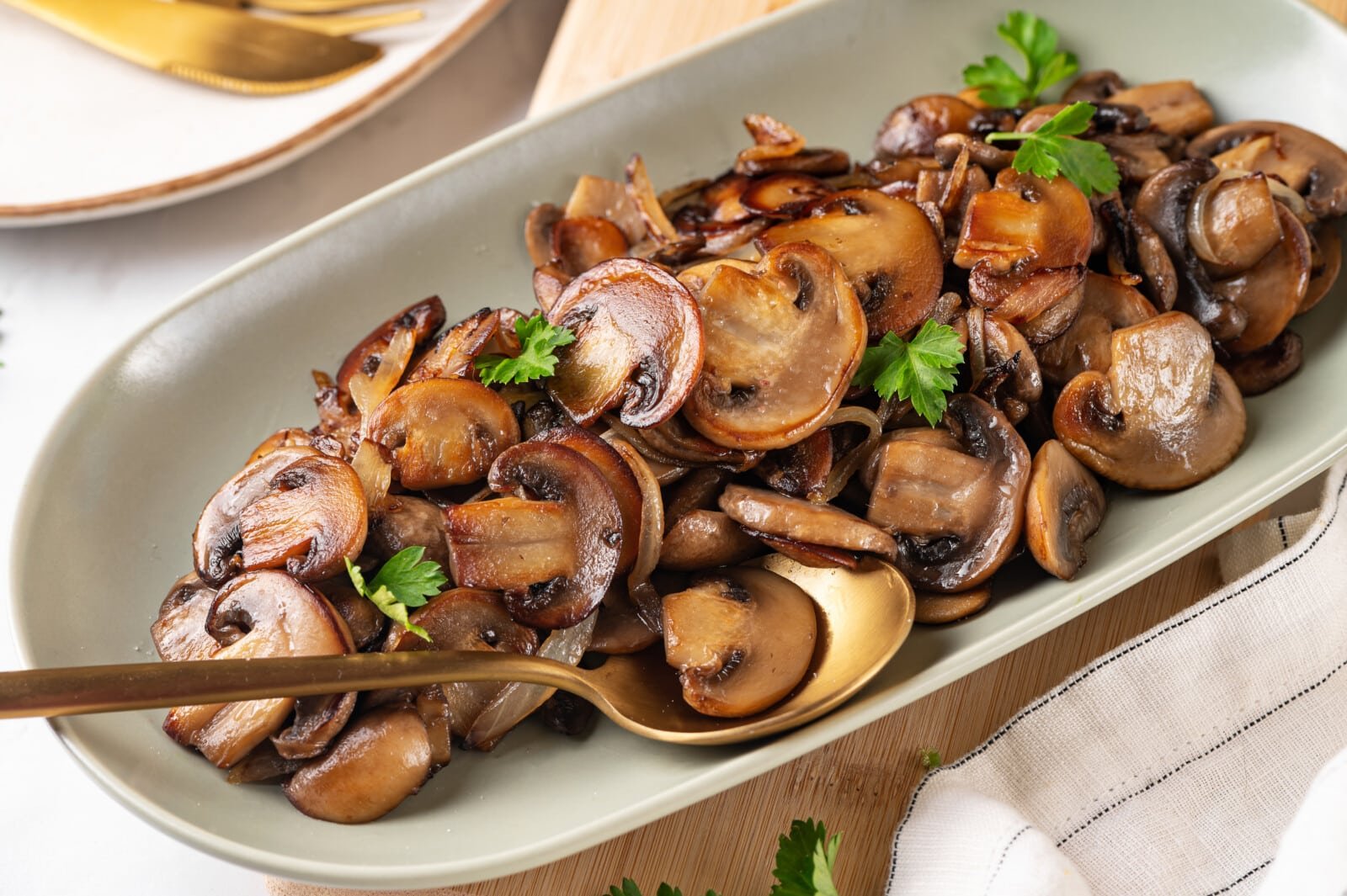 Serving sautéed mushrooms on a white plate with leaves of parsley.