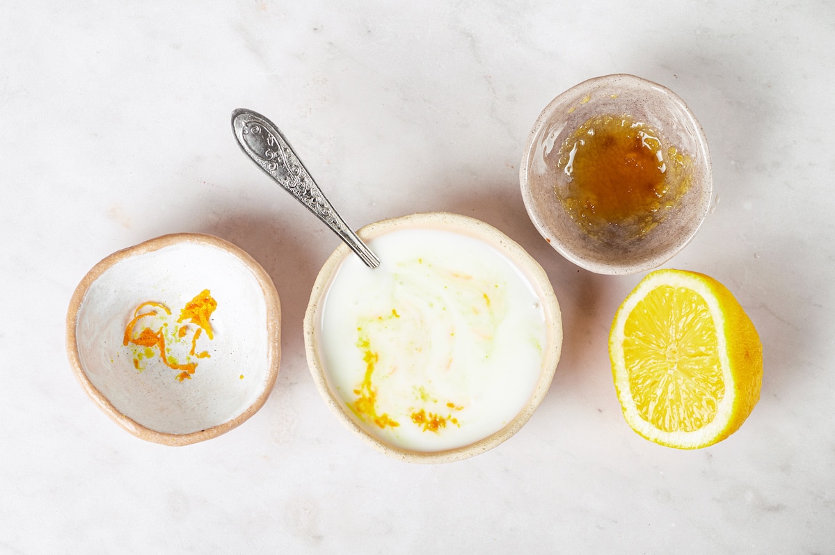 honey orange zest yogurt and lemon sliced combined into one cream bowl with silver spoon.