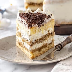 Tiramisu cake slice on a white speckled plate with a fork.