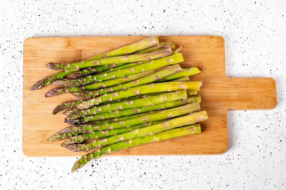 stalks of fresh raw green asparagus on a wooden board.