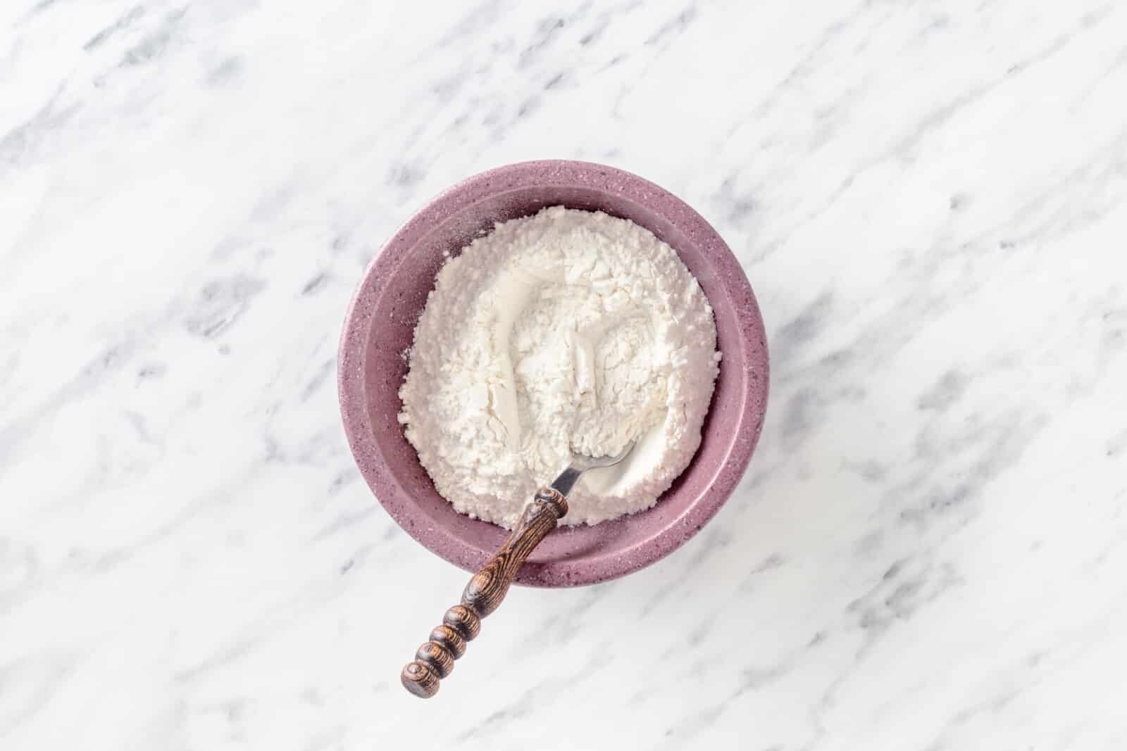 Two flours combining in a purple bowl with a spoon.