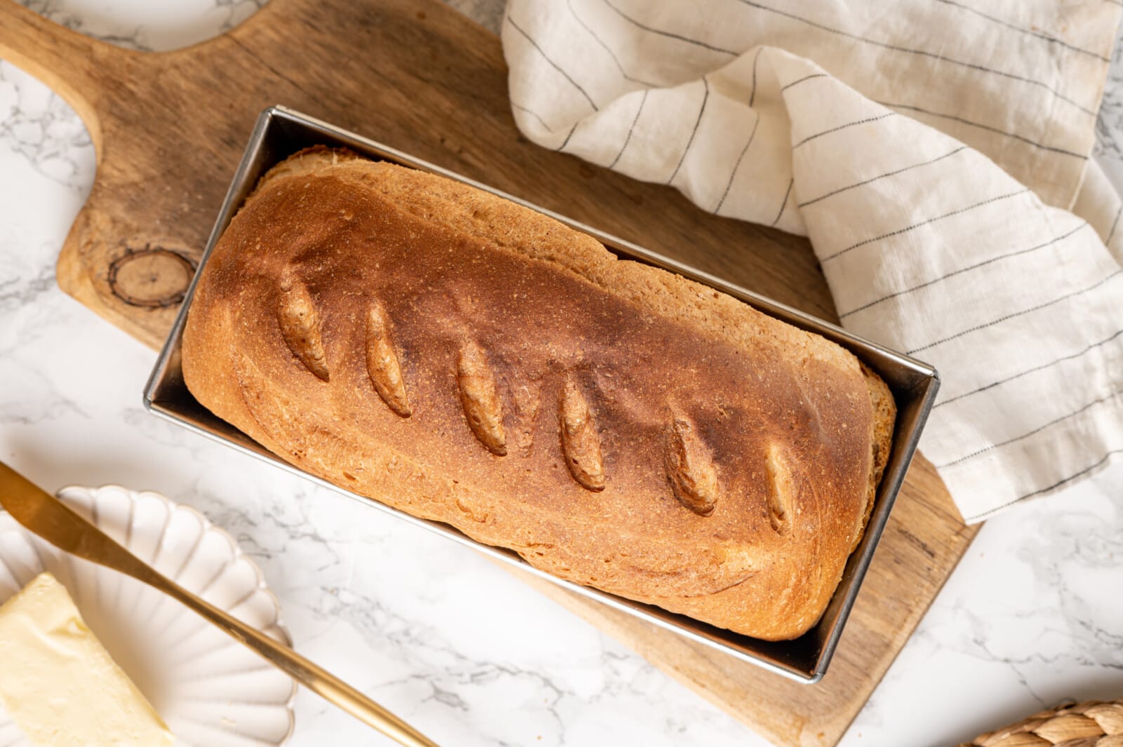 Whole wheat bread baked in a loaf pan atop a wooden board.