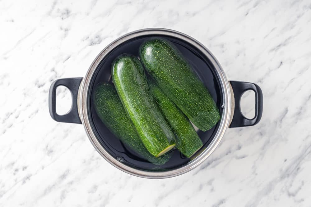 whole zucchinis in a silver pot filled with water.