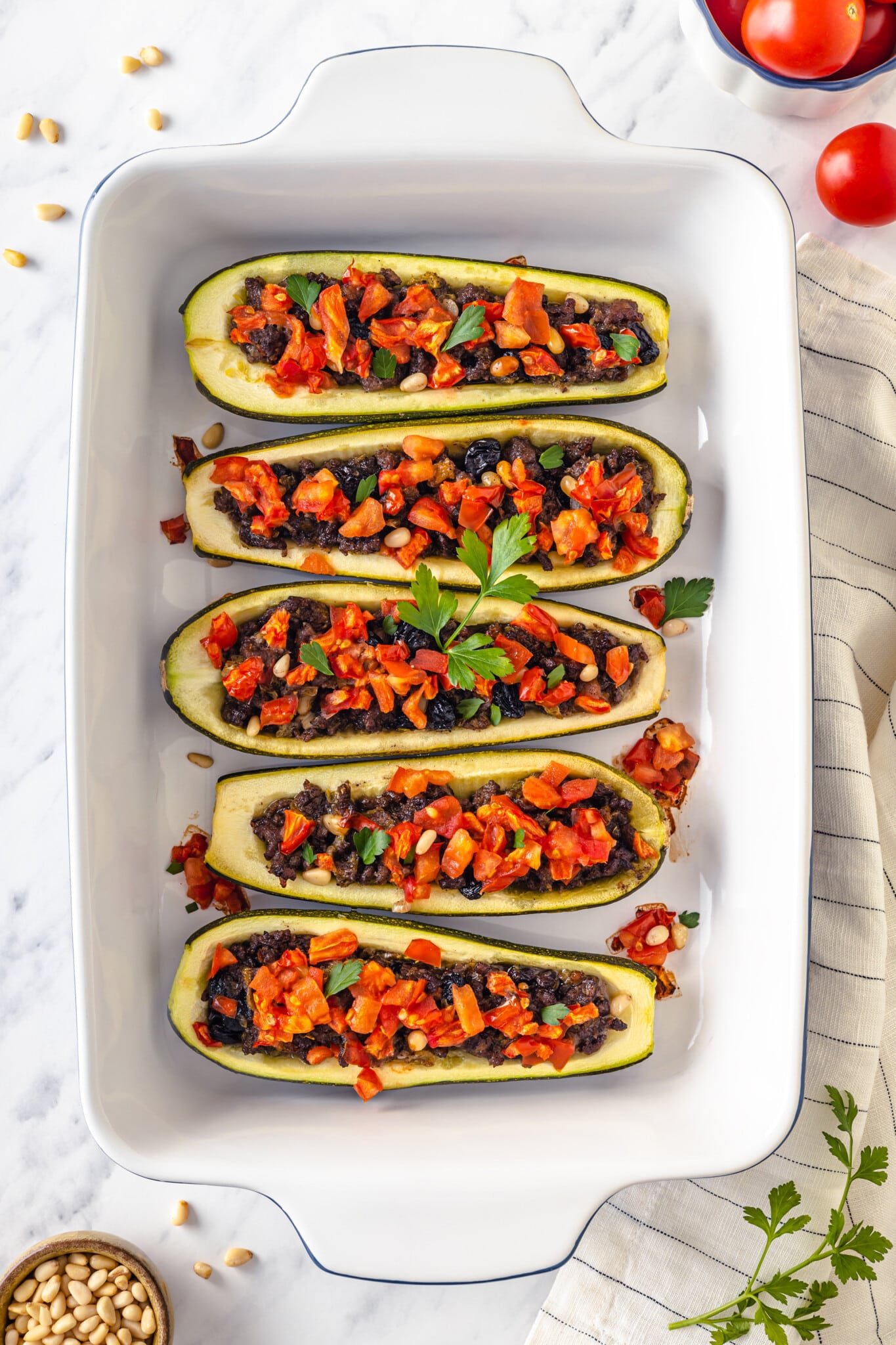 stuffed zucchini boats lined up in a baking dish with garnish and tomatoes on top 