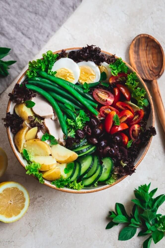 nicoise-salad-in-a-bowl-with-a-wooden-spoon-and-lemon-the-side