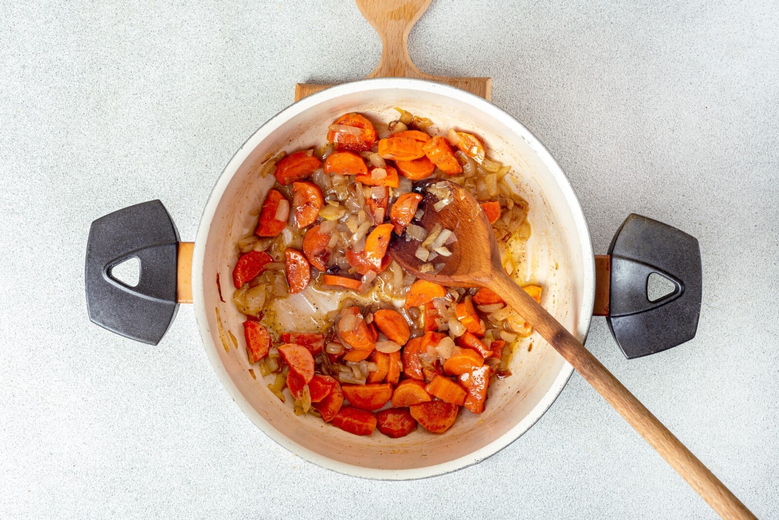 carrots and onion sauteing in a pot on a cutting board with a spoon.