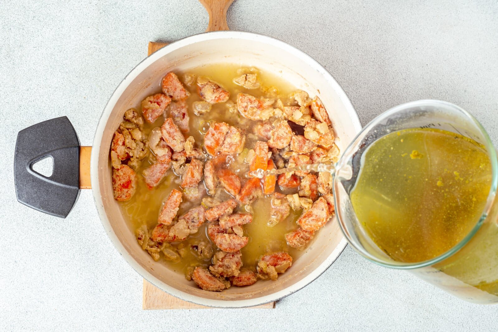 sauteed ingredients in a soup pot adding broth from a glass dish.