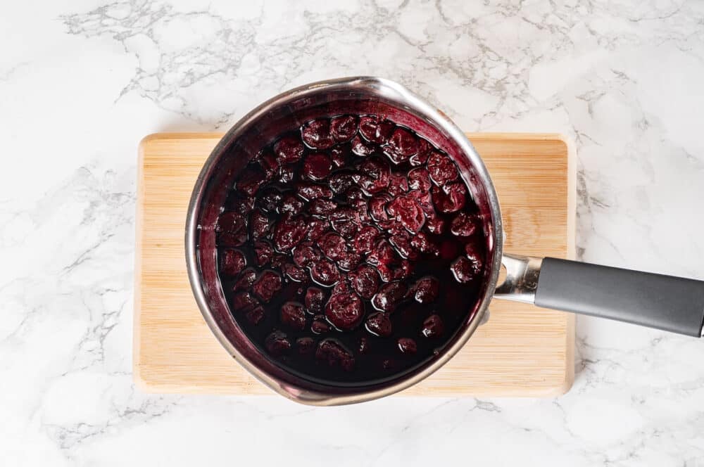 cooked and boiled red cherry jam on a wooden board on white marble background.