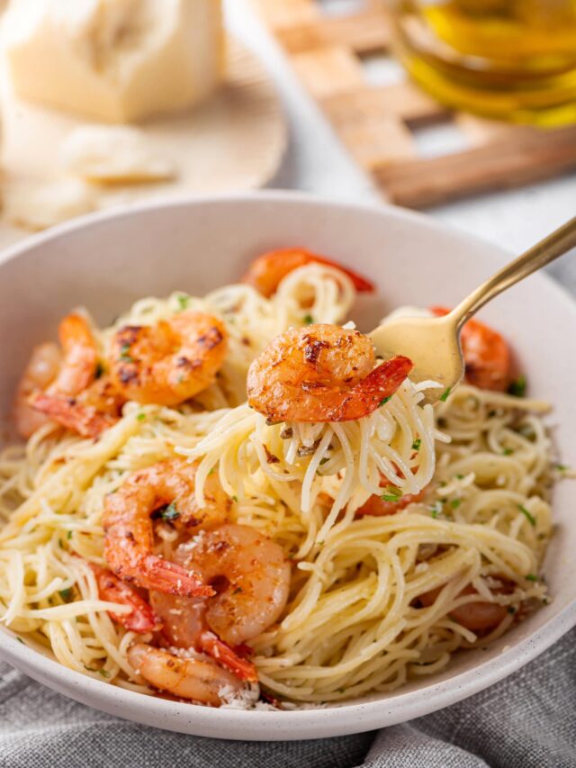 capellini shrimp in a white bowl with shrimp and a gold fork on a brown towel.