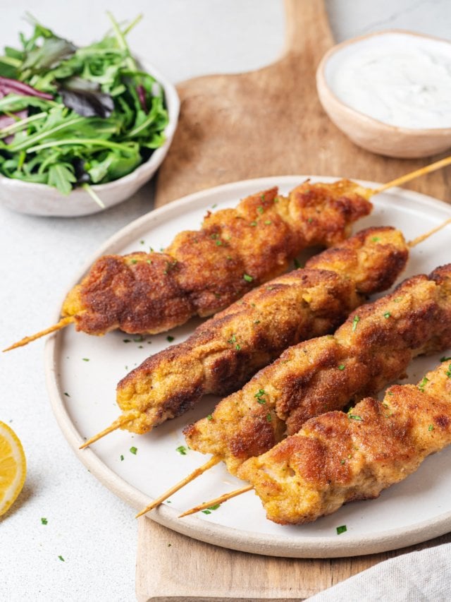 chicken-skewers-on-a-white-plate-wooden-board-greens-in-a-bowl