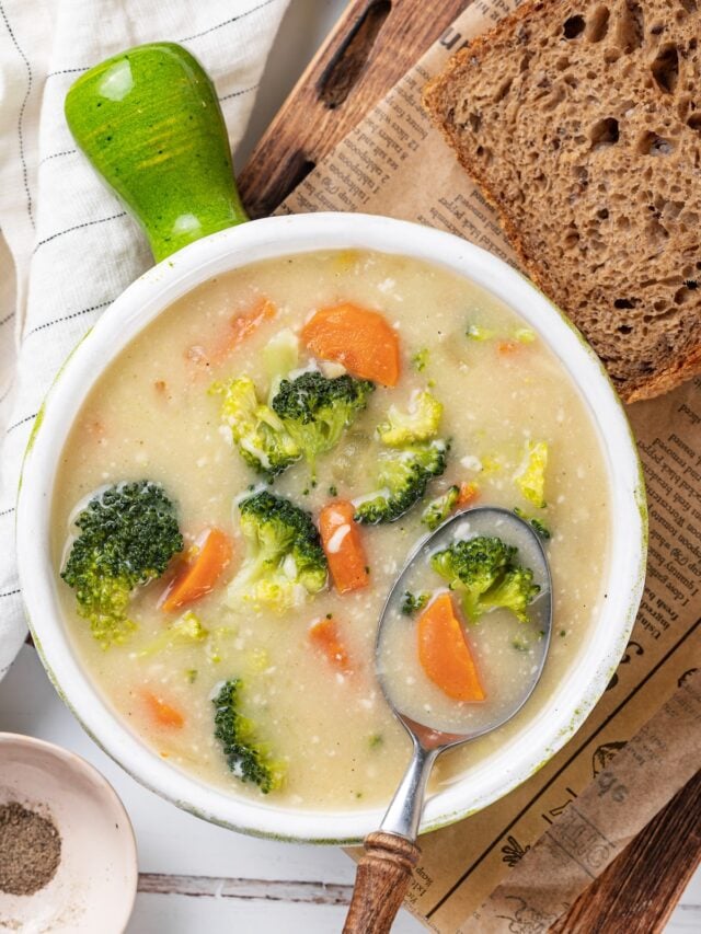 broccoli soup with cheese in a bowl with a green handle with a spoon in the bowl and a piece of black bread on the side.
