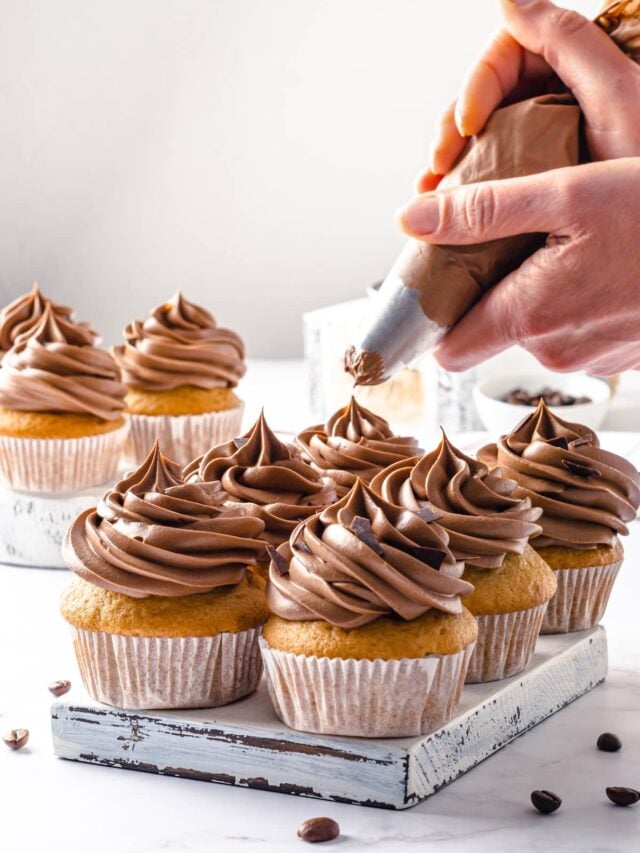 frosting coffee cupcakes with frosting in a piping bag.