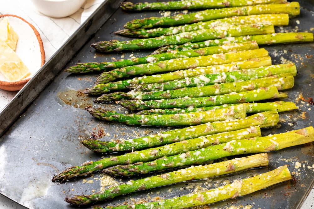 roasted stalks of asparagus with melted parmesan on top on a grey baking sheet.