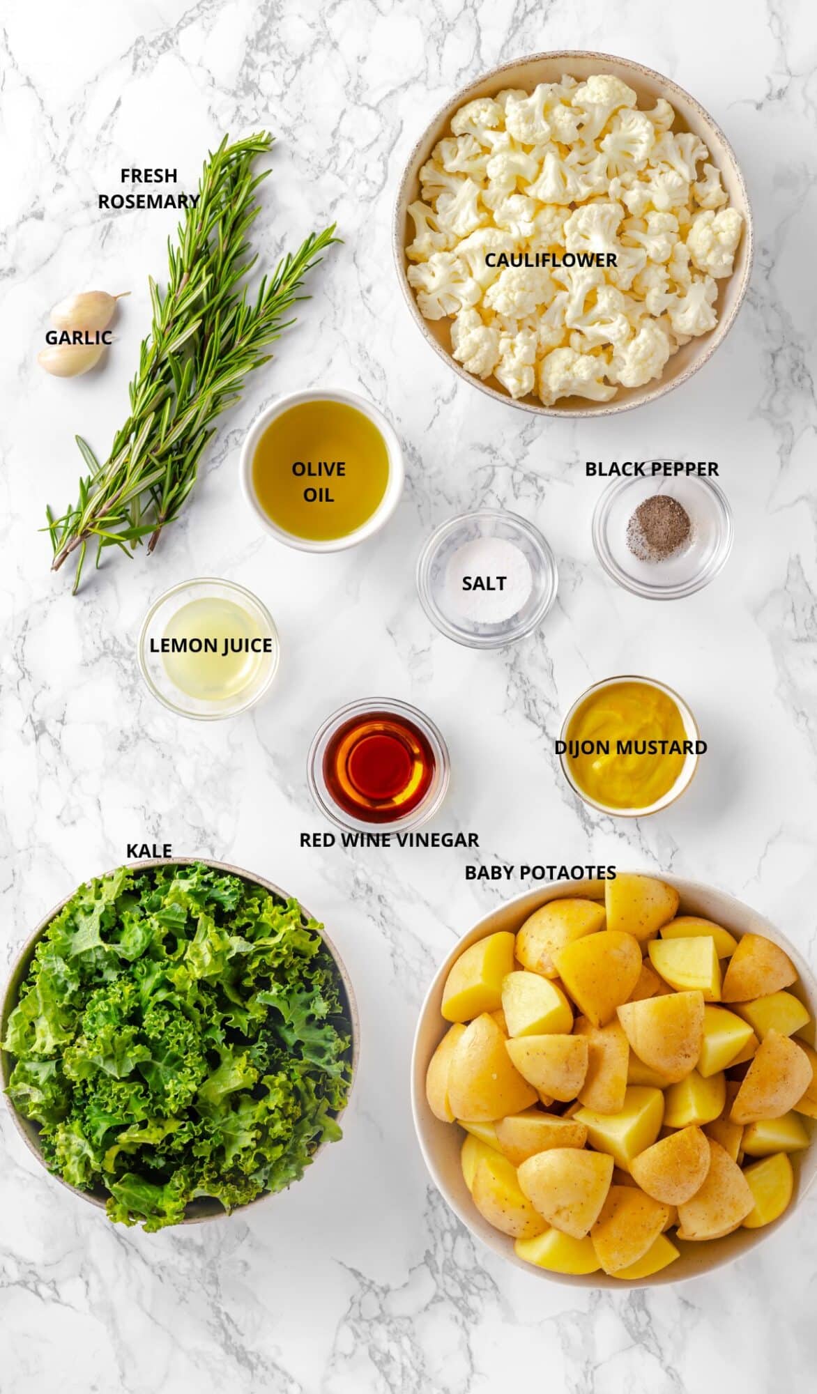 potatoes, kale, cauliflower, rosemary, garlic, olive oil, mustard, vinegar, salt and pepper laid out for roasting potatoes. 