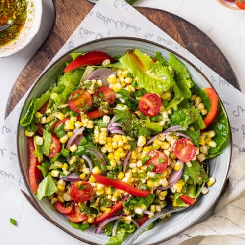 Smoked corn salad in a large bowl displayed atop a wooden cutting board with a spoon for serving.