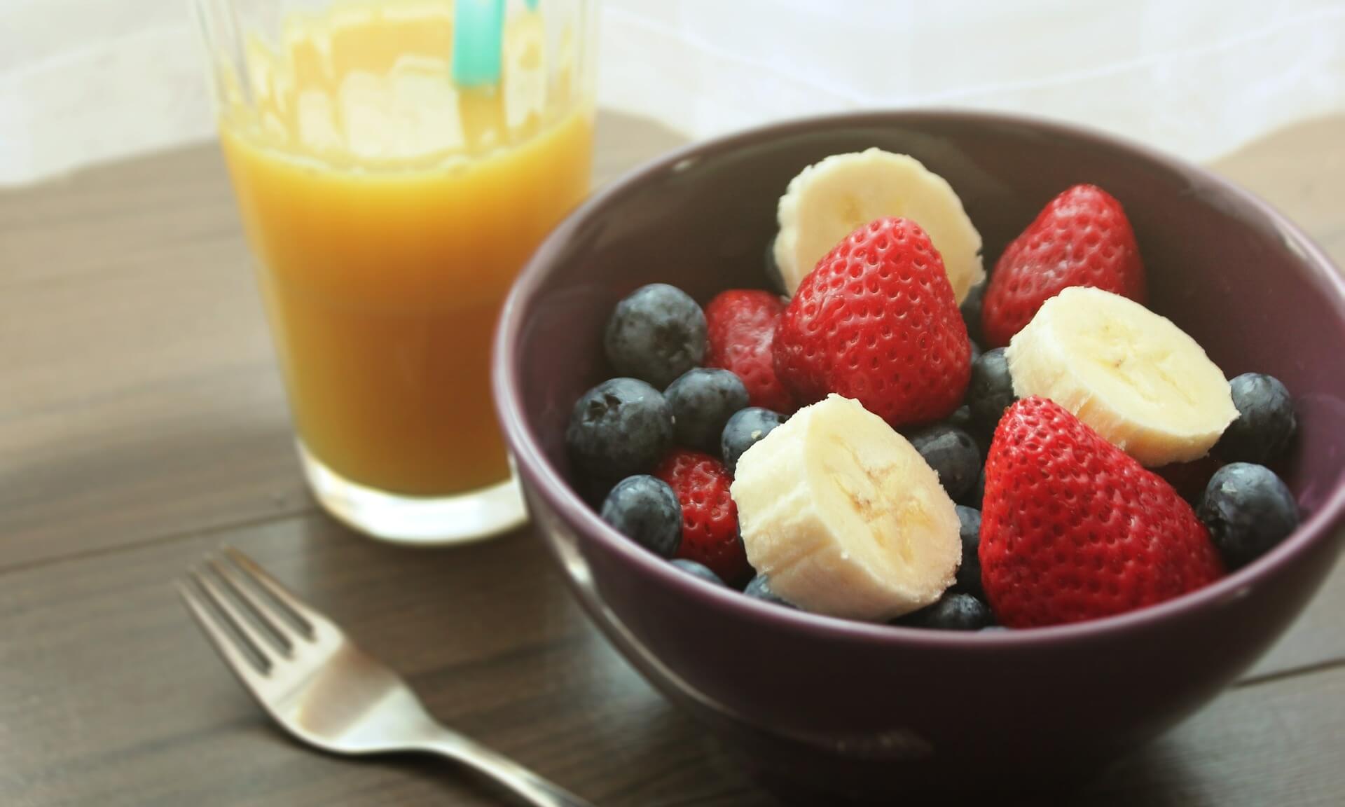 fruits-in-a-bowl-with-a-fork-and-a-glass-of-orange-juice-on-the-side