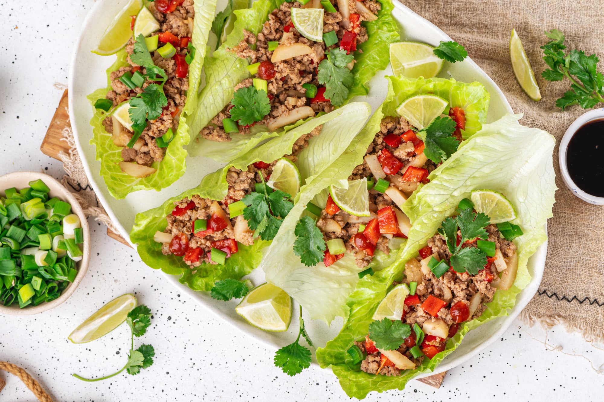 Top view of turkey lettuce wraps prepared with lime wedges and laid out on a white plate.