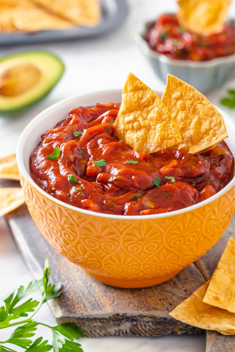 red salsa in a white bowl with a yellow decorated outside on a board with chips in the salsa.