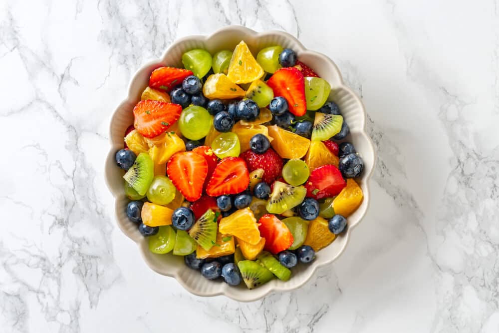 bowl of fruit mixed in a white bowl on marble background.