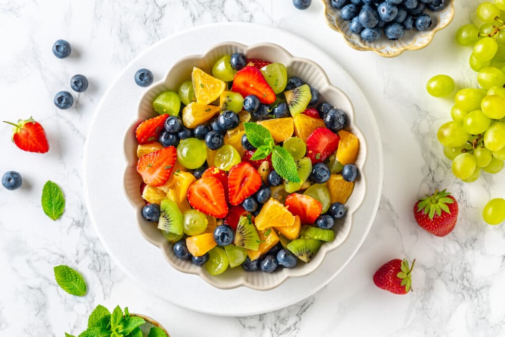 bowl of fruit on a white background with blueberries and strawberries and fresh mint around.