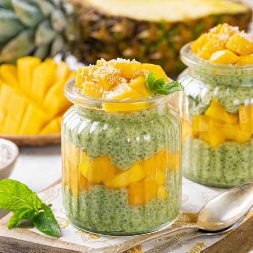 mango and spinach chia seed pudding in two jars with shredded coconut on the top, on a wooden board and parchment paper.
