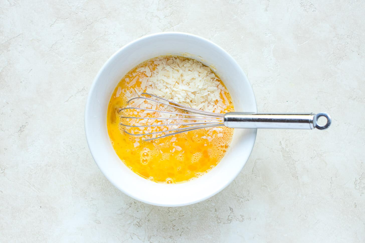 Whisked eggs with cheese in a white bowl with a whisk. 