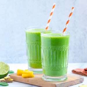 mango-pineapple-smoothie-in-glasses-with-straws-on-a-wooden-board-with-ingredients-on-the-side