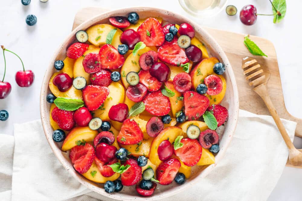 Summer fruit salad in a bowl with ingredients for the salad around.