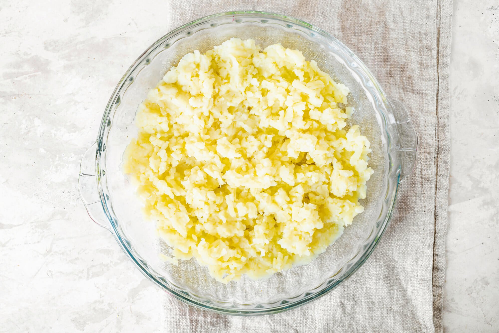 potato-layer-on-herring-salad-in-a-glass-baking-dish-on-a-white-towel