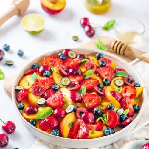 Summer fruit salad in a bowl with ingredients for the salad around.