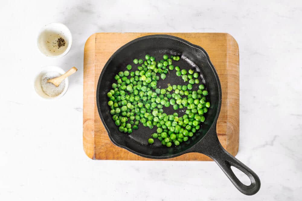 peas-in-a-skillet-on-a-wooden-board-with-two-small-white-bowls-on-the-side
