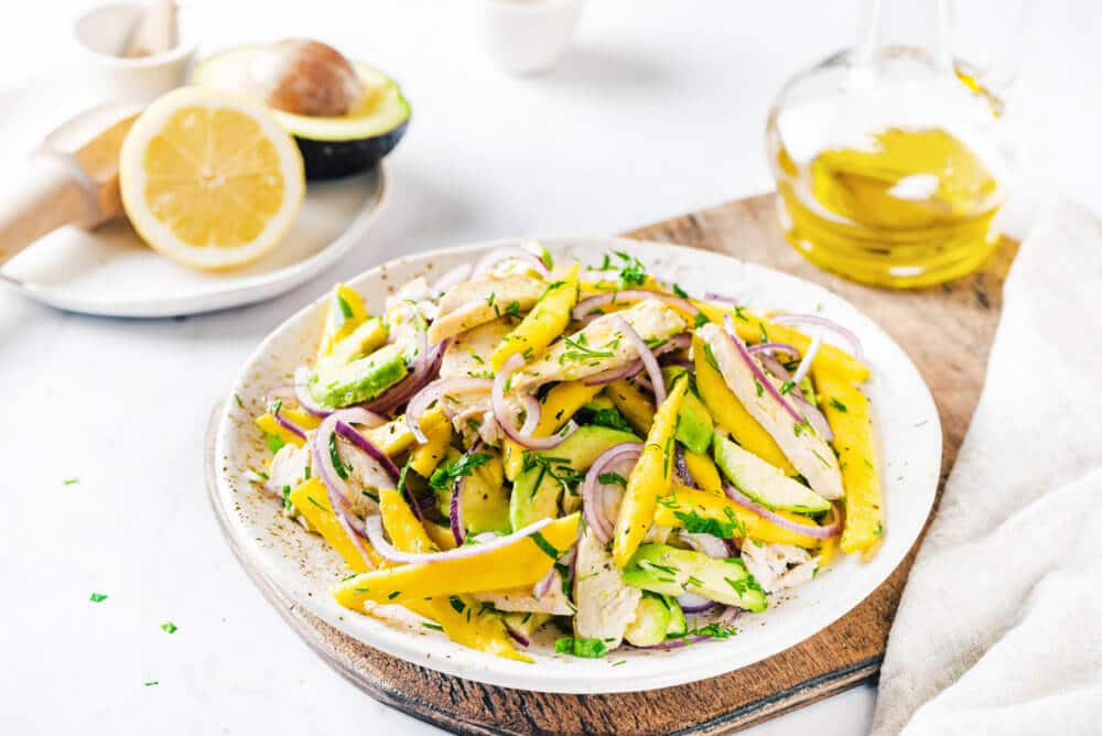 avocado chicken mango salad on a white plate on a wooden board.