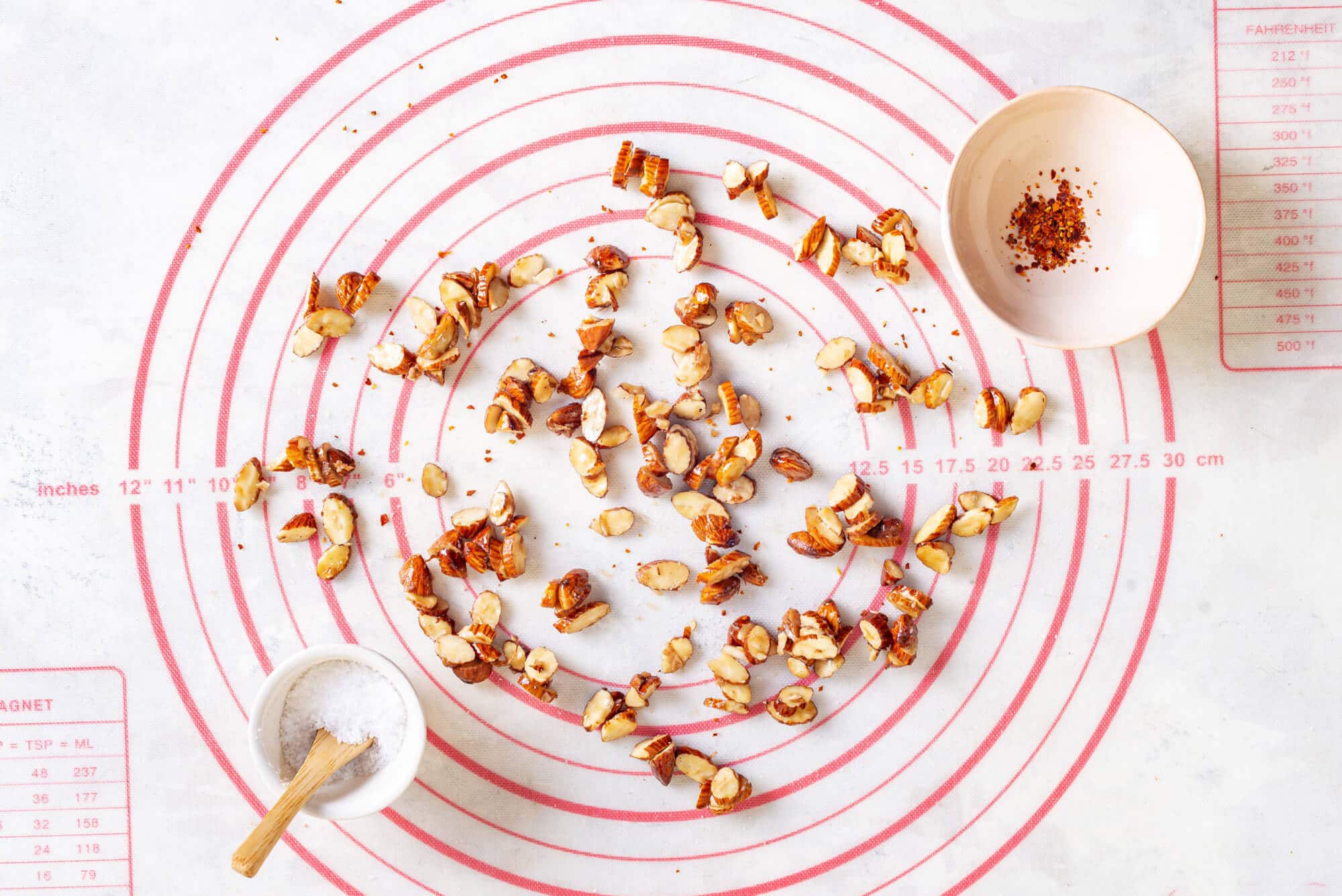 Chopped almonds on a baking tray with a bowl of salt and a bowl of chili flakes on the side.