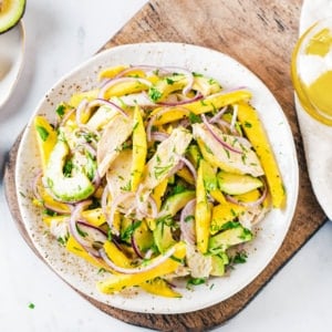 avocado-chicken-mango-salad-on-a-white-plate-on-a-wooden-board-with-olive-oil-and-a-lemon-wedge-on-the-side