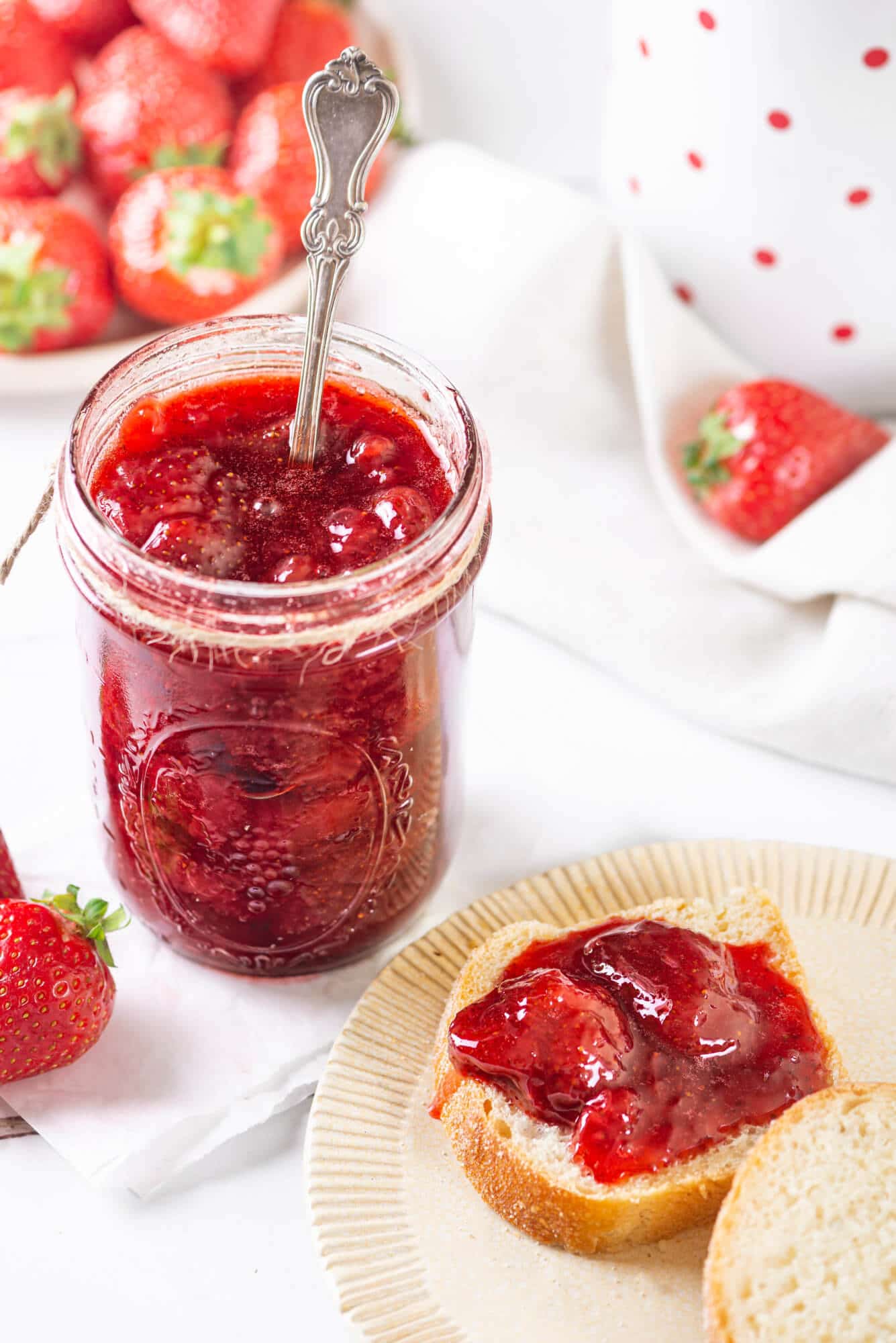 strwaberry-jam-in-a-jar-with-a-spoon-with-toast-on-a-plate-with-jam-on-it-and-strawberries-in-the-background
