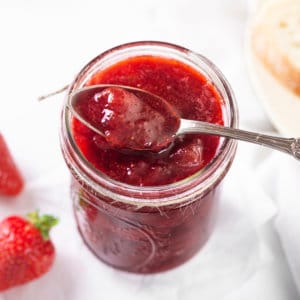 strawberry-jam-in-a-glass-jar-with-a-silver-spoon-with-jam-and-strawberries-in-the-background