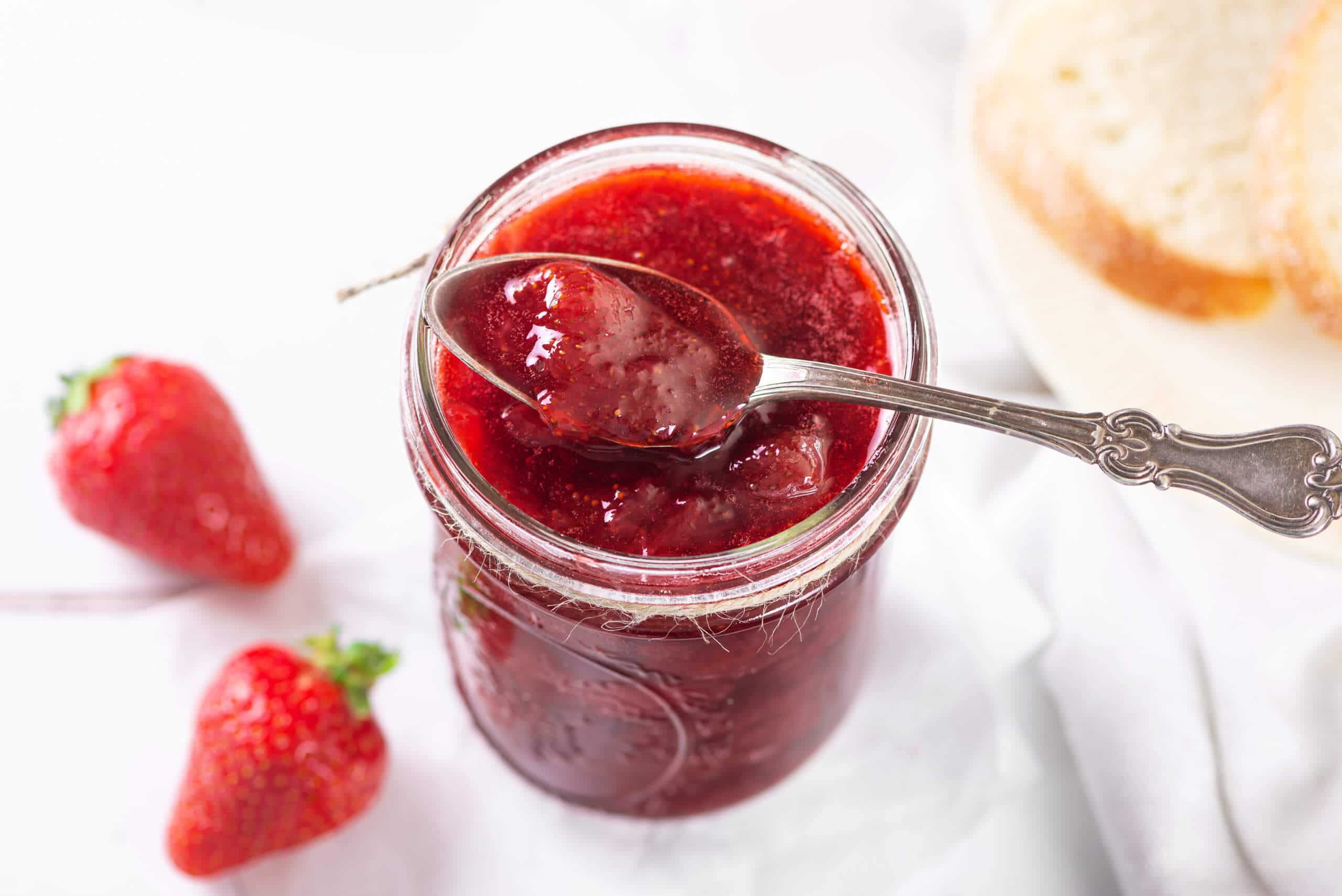 strawberry-jam-in-a-glass-jar-with-a-silver-spoon-with-jam-and-strawberries-in-the-background
