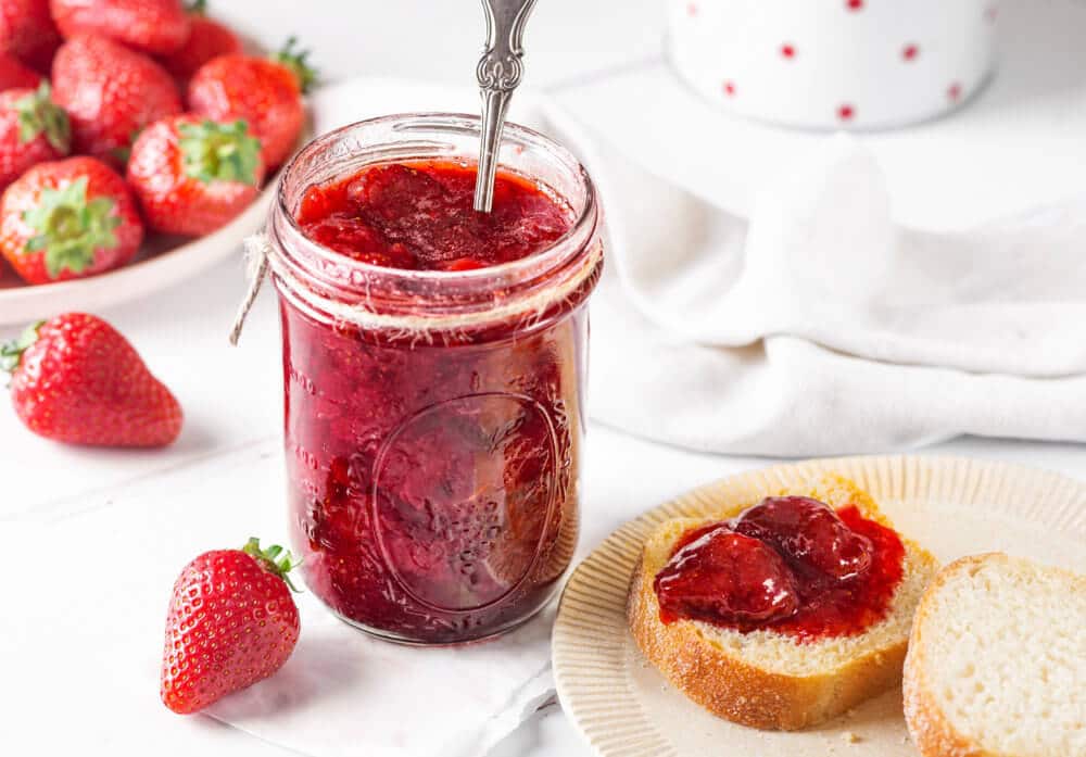 strwaberry-jam-in-a-jar-with-a-spoon-with-toast-on-a-plate-with-jam-on-it-and-strawberries-in-the-background