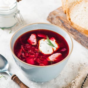 wooden-board-white-bread-white-bowl-red-borscht-sour-cream-dill-clear-bowl-with-sour-cream-and-a-wooden-spoon-brown-towel
