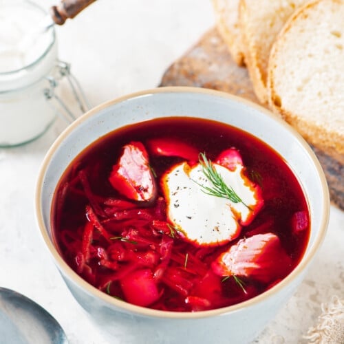 A bowl of borscht with a dollop of sour cream on top with a spoon on the side.