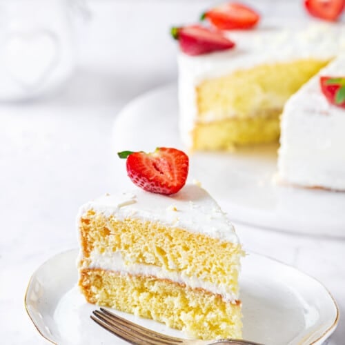 biskvit-cake-slice-on-a-white-plate-with-the-rest-of-the-cake-in-the-background-with-a-fork-on-the-side
