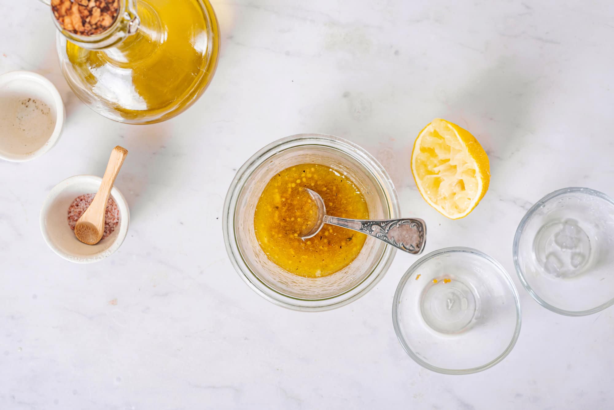 Dressing in a glass bowl with a spoon, with some lemon, olive oil, and salt dishes on the side.