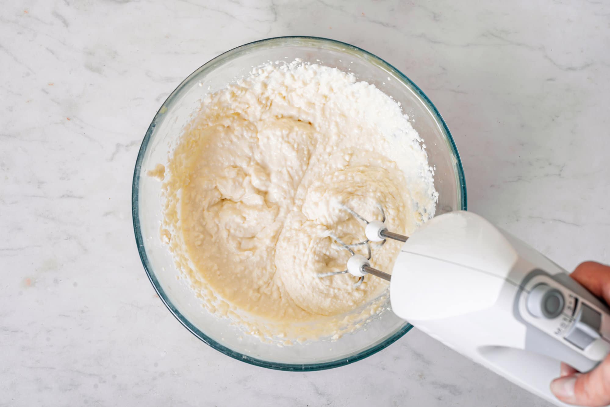 Blueberry cheese cake batter being mixed with a handheld mixer. 