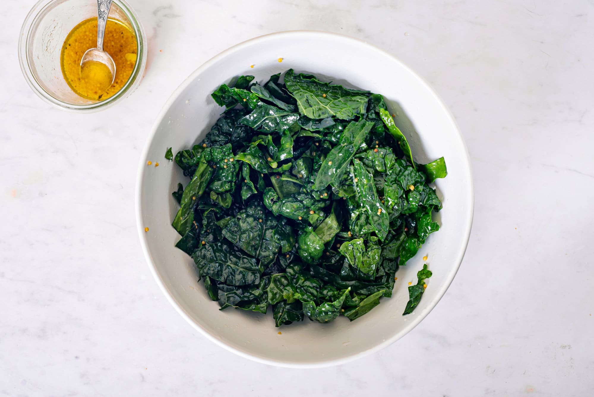 A white bowl of kale salad, with a dressing bowl on the side.