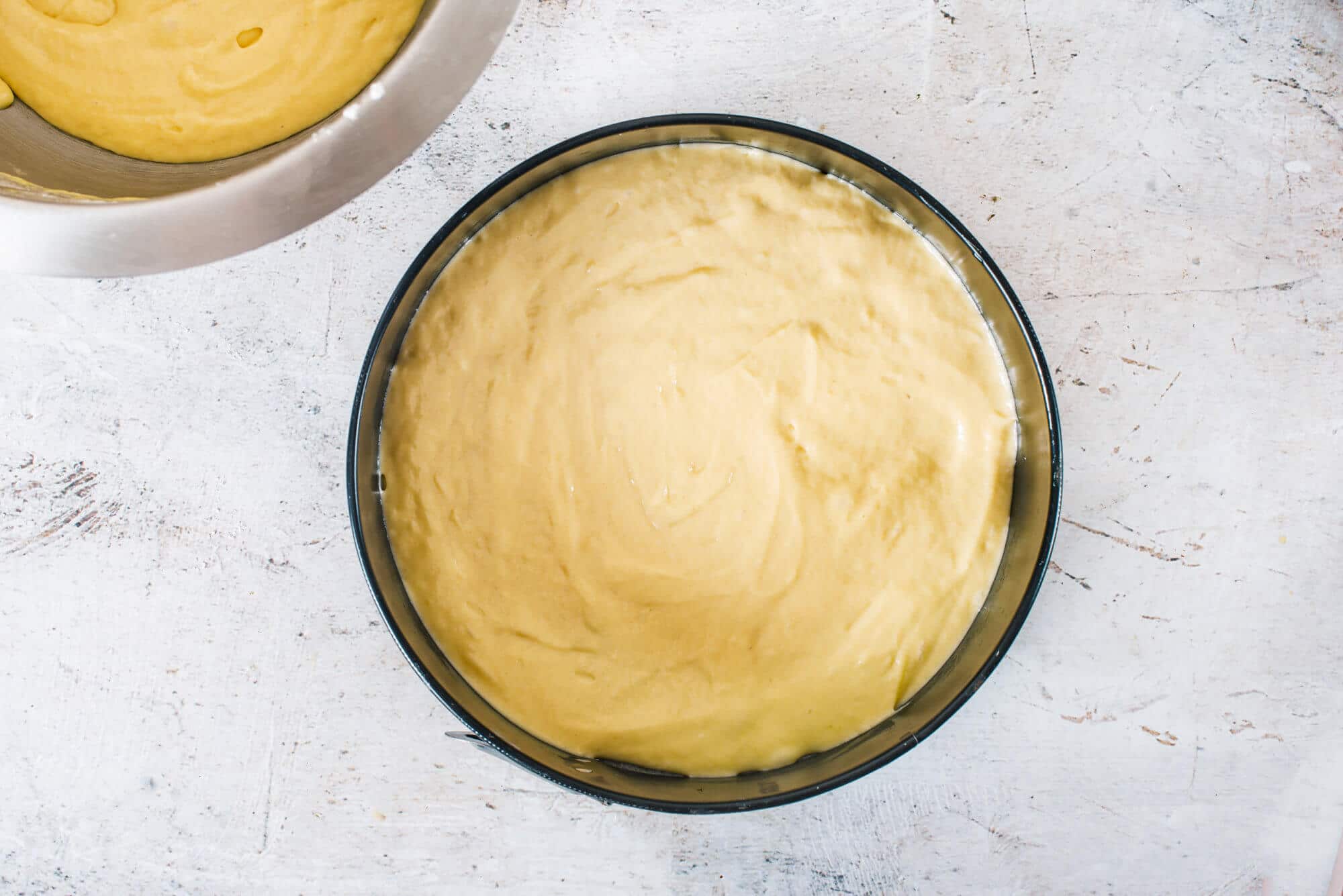 vanilla-cake-batter-in-a-springform-pan-with-a-silver-bowl-of-batter-on-the-side