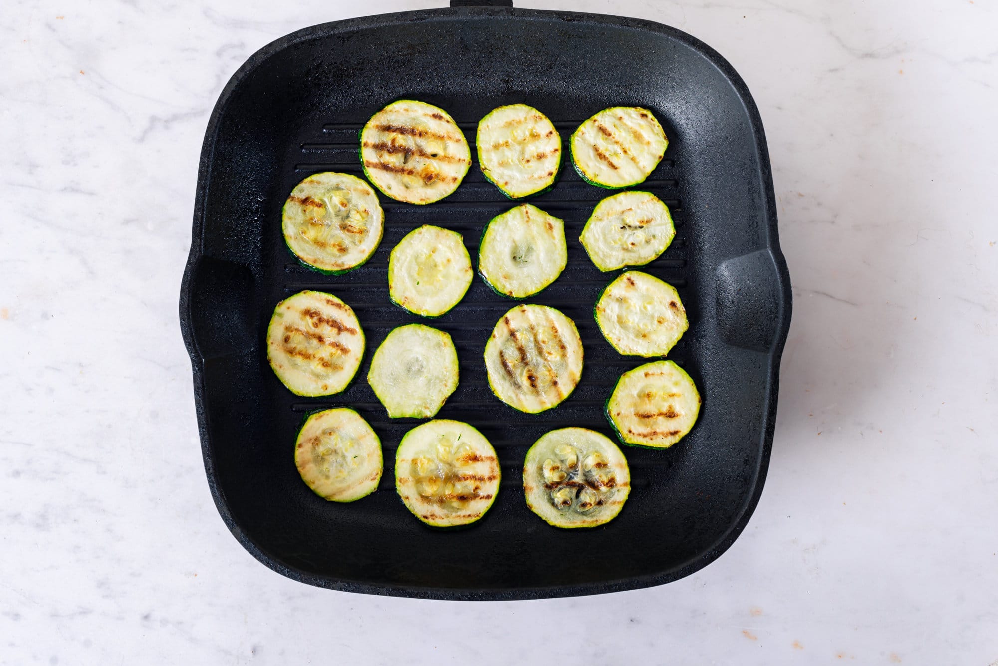 Sliced zucchini grilling on a pan. 