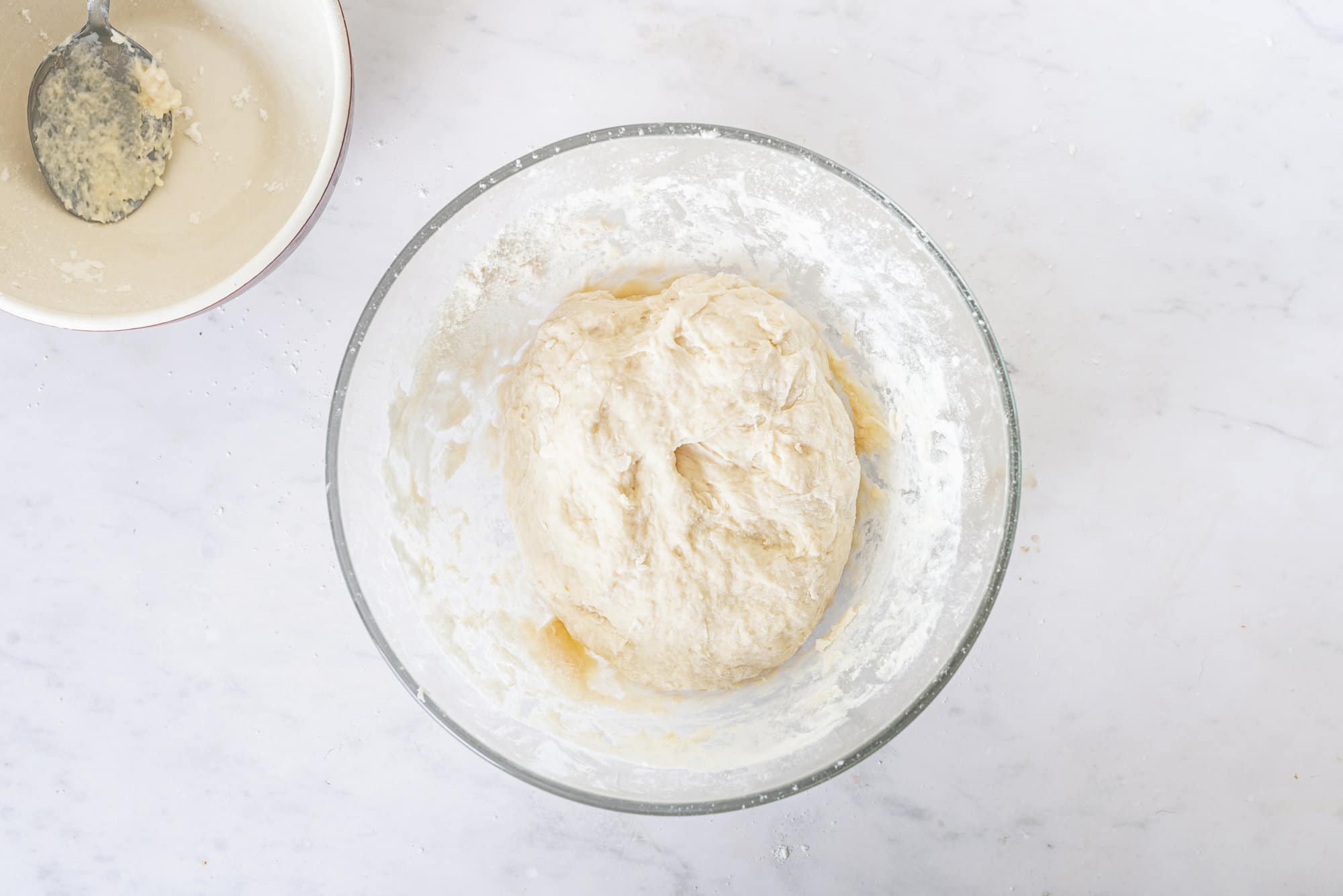 dough-in-a-glass-bowl-with-a-beige-bowl-on-the-side-with-a-spoon-in-it