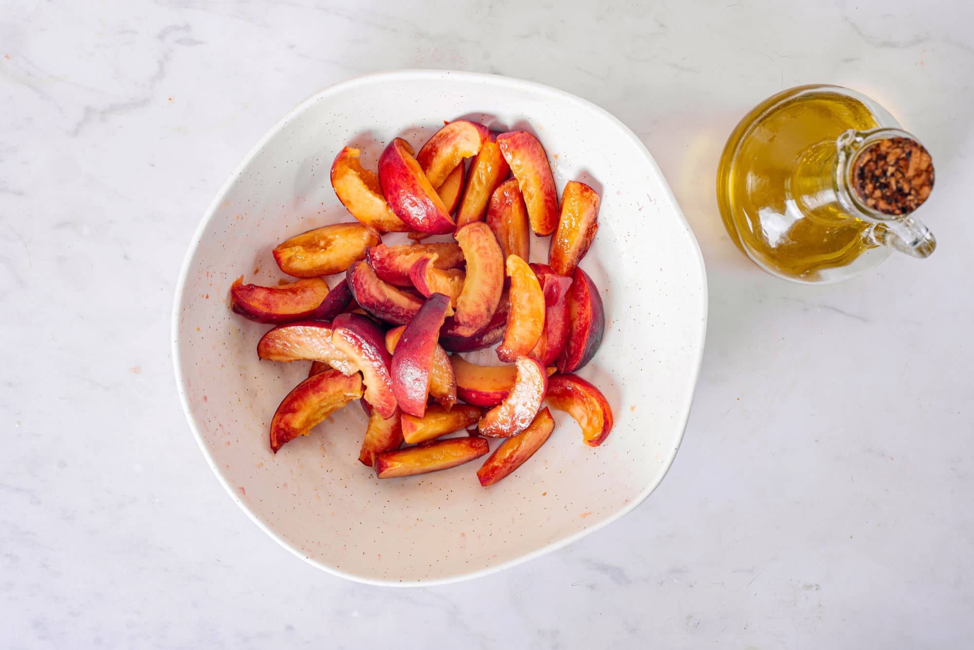 Sliced peaches in a white bowl with a dish of olive oil on the side.