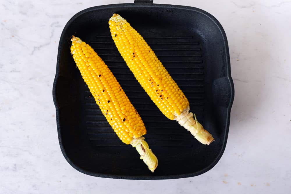 Corn on the cob grilling on a pan.