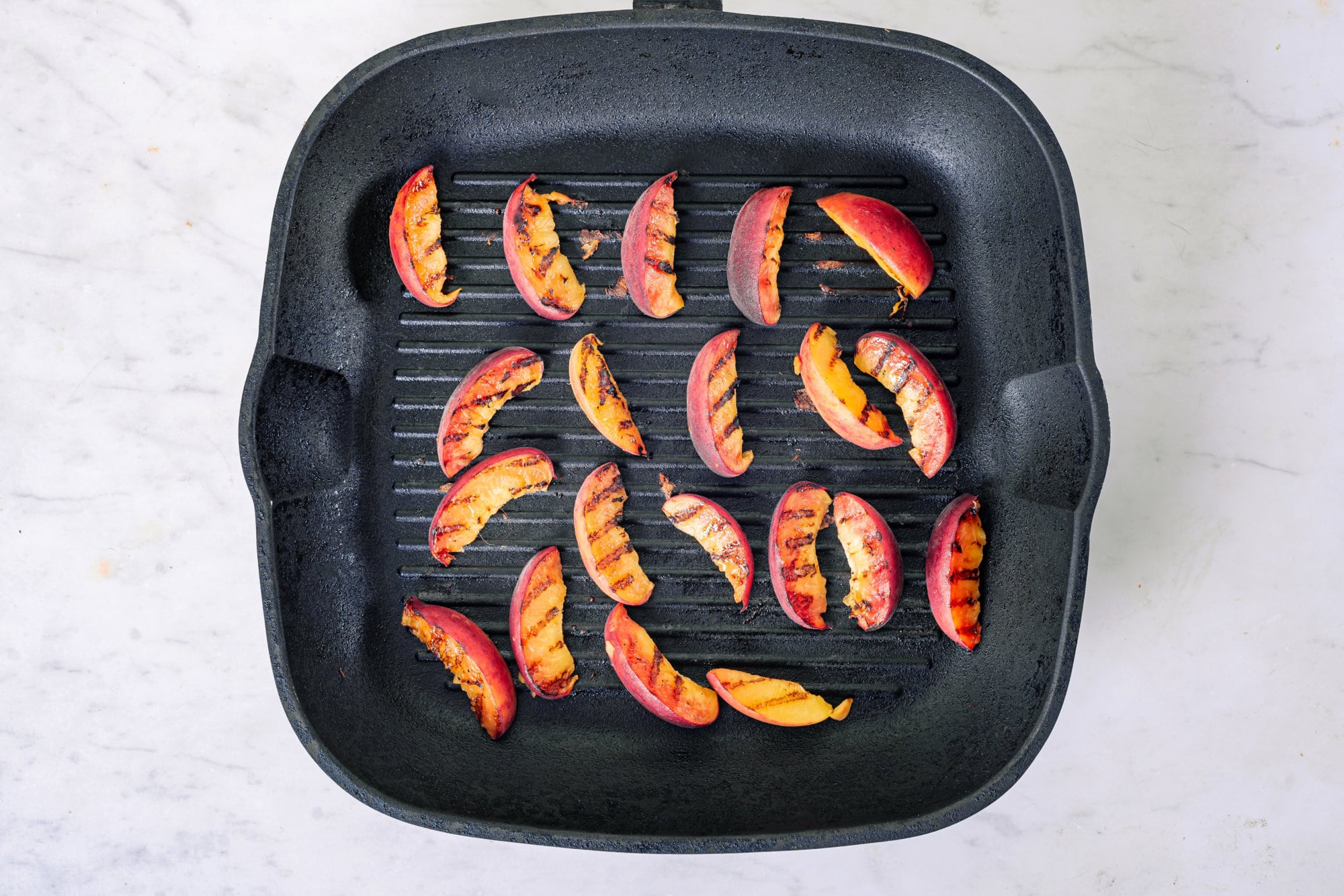 Peaches grilling in a square black skillet.